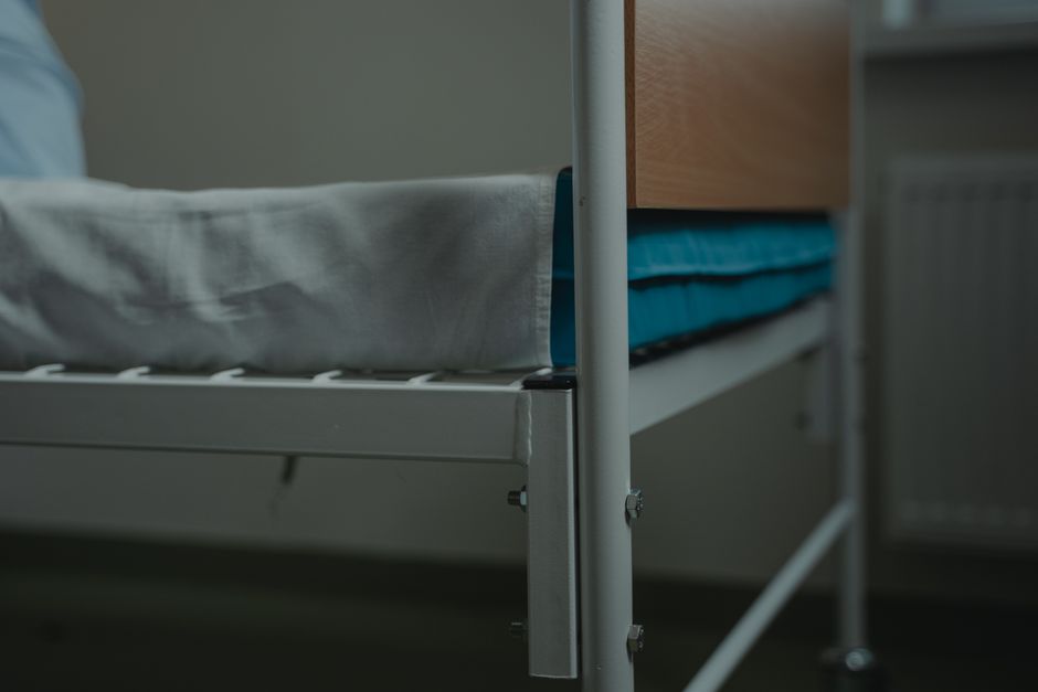 Close-up view of a hospital bed with white linens and metal frame, indoors.
