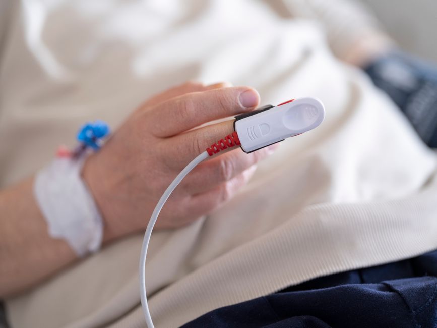 Detailed image of a patient's finger with a pulse oximeter in a hospital setting.