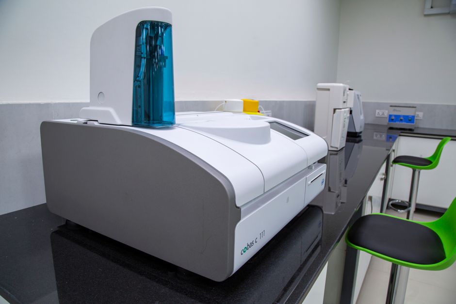 Technician inspecting a compact laminate cross-section with a thickness gauge during medical furniture material compliance testing